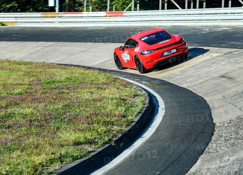 View from the perspective of a racing driver on a red sports car Porsche Cayman from nuerburgring.de driving through the Caracciola-Karrussell Caracciola Karrussell Caracciola Karrussell narrow bend with a steep incline on the Nürburgring race track Nordschleife Green Hell Green Hell historic international official race track for motorsport in the Eifel, Nürburg, Rhineland-Palatinate, Germany, Europe