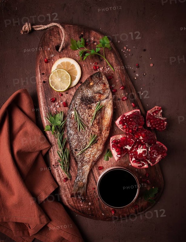 Fried dorado fish, with spices and herbs, on a wooden board, pomegranate sauce, close-up, no people