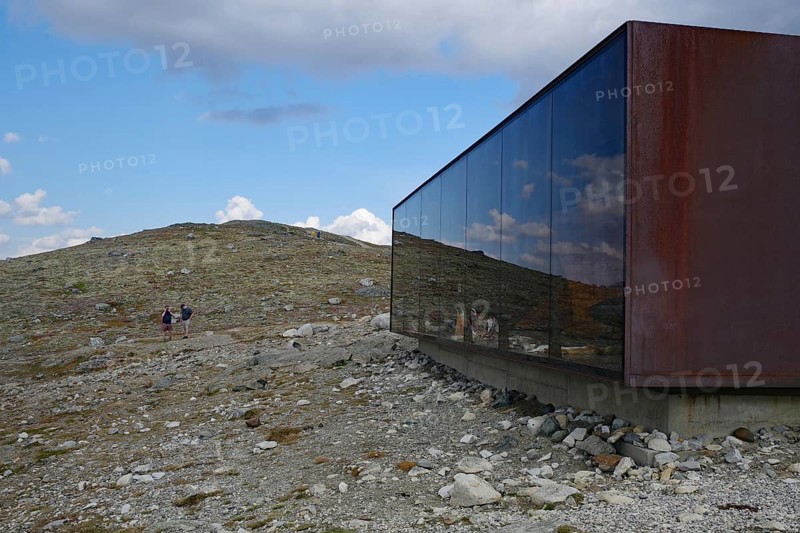 Modern glass building in a mountainous landscape with hikers in the distance, Snöhetta viewpoint and shelter, Hjerkinn, Dovrefjell-Sunndalsfjella National Park, Norway, Europe