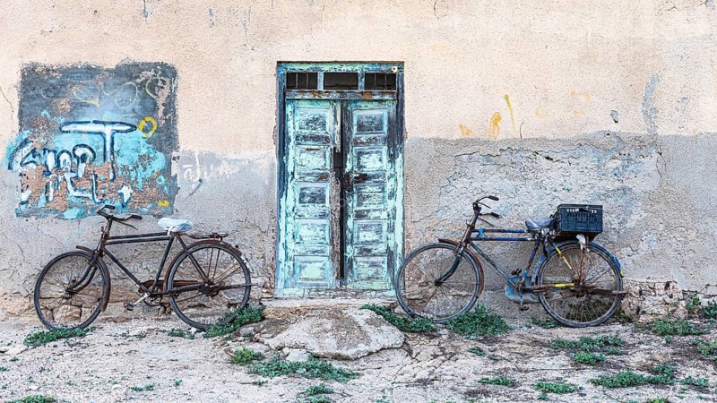 Old bicycles leaning against a house wall with an old wooden door, on the beach of Salalah, Dhofar Province, Arabian Peninsula, Sultanate of Oman