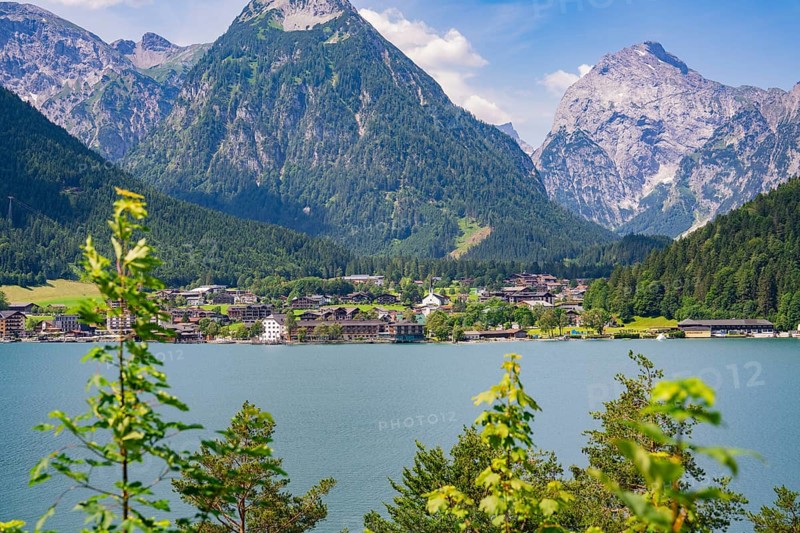 Lake surrounded by green mountains with a small cluster of houses in the sunlight, Achernsee, Austria, Germany, Europe
