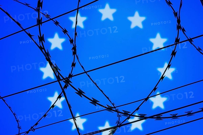 Symbolic image, migration, defence against refugees wanting to enter the EU, barbed wire overarches the stars of the EU flag against a blue sky, border, border fence