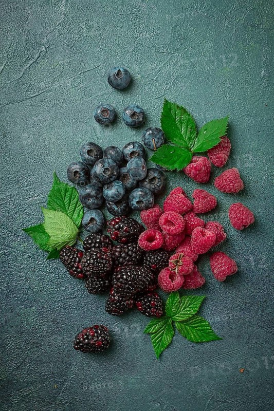A mix of ripe berries, with leaves scattered on the table, raspberries, blackberries, blueberries, food background