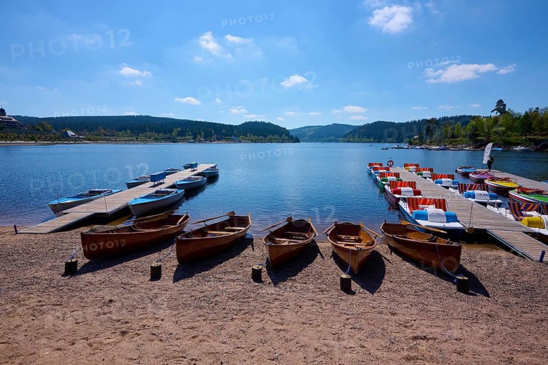 A picturesque scene with colourful pedal boats and wooden boats on a jetty in front of the Schluchsee, surrounded by mountains, spring, Schluchsee, Black Forest, Baden-Württemberg, Germany, Europe