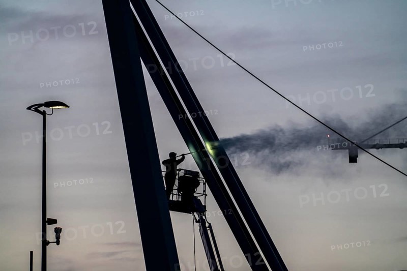 Worker cleans a bridge pier with a high-pressure cleaner on a cherry picker at the Erasmus Bridge over the Nieuwe Maas in Rotterdam, Netherlands