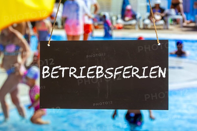 Symbolic image of company holidays: Sign with the inscription BETRIEBSFERIEN in front of summer holidaymakers in the outdoor pool (Composing)