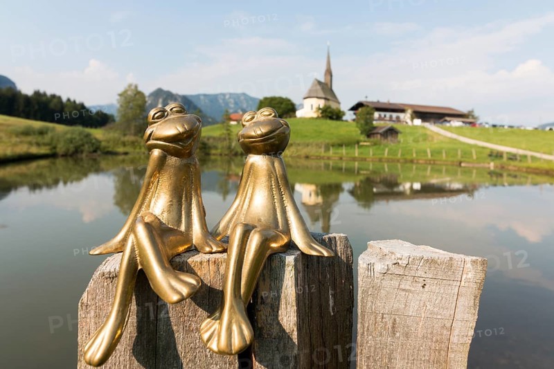 Two brass frogs, behind them the church of St Nicholas, Einsiedl, Inzell, Bavaria, Germany, Europe