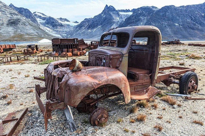 Rusted car and oil drums in front of steep mountains, remains of a US airbase from the Second World War, Ikateq Fjord, East Greenland, Greenland, North America