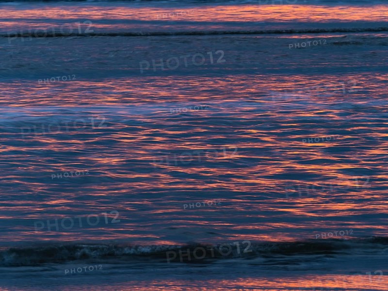 Abstract image of the North Sea, a evening mood with colorful pink reflections of the setting sun, on the water as it reaches the beach, island of Texel, Holland