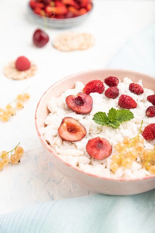 Rice flakes porridge with milk and strawberry in ceramic bowl on white concrete background and blue linen textile. Side view, close up, selective focus