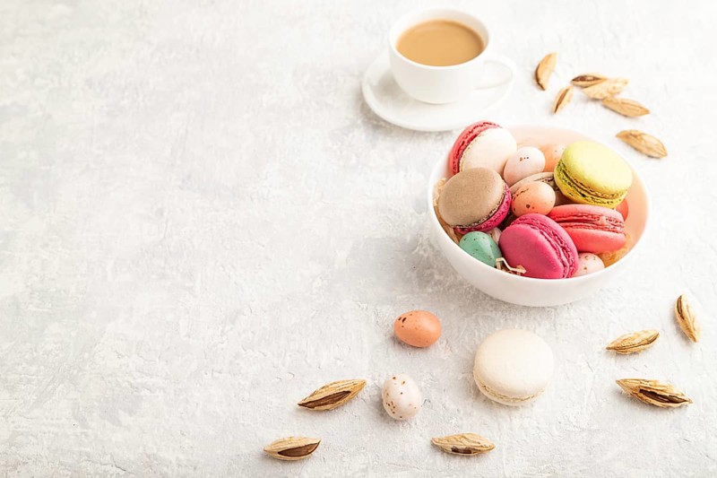 Multicolored macaroons and chocolate eggs in ceramic bowl, cup of coffee on gray concrete background. side view, copy space, still life. Breakfast, morning, concept