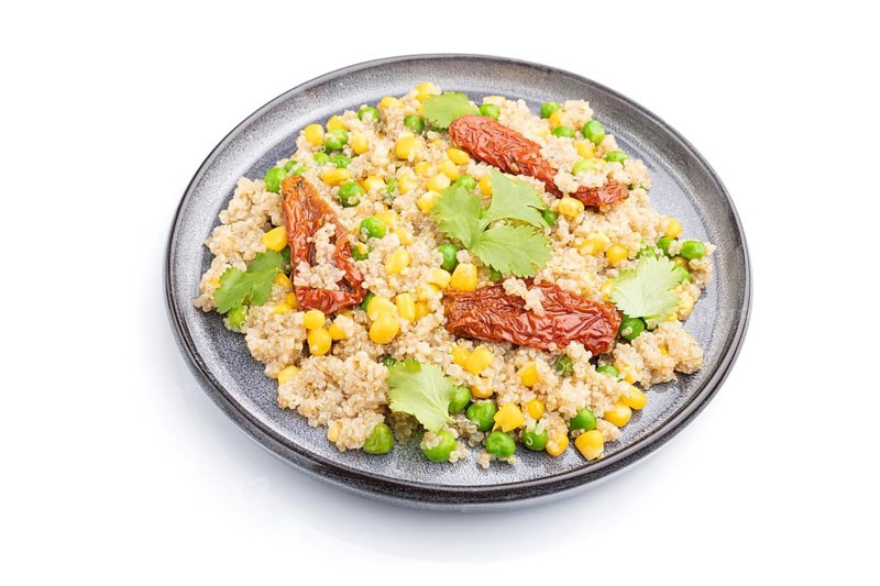 Quinoa porridge with green pea, corn and dried tomatoes on ceramic plate isolated on white background. Side view, close up
