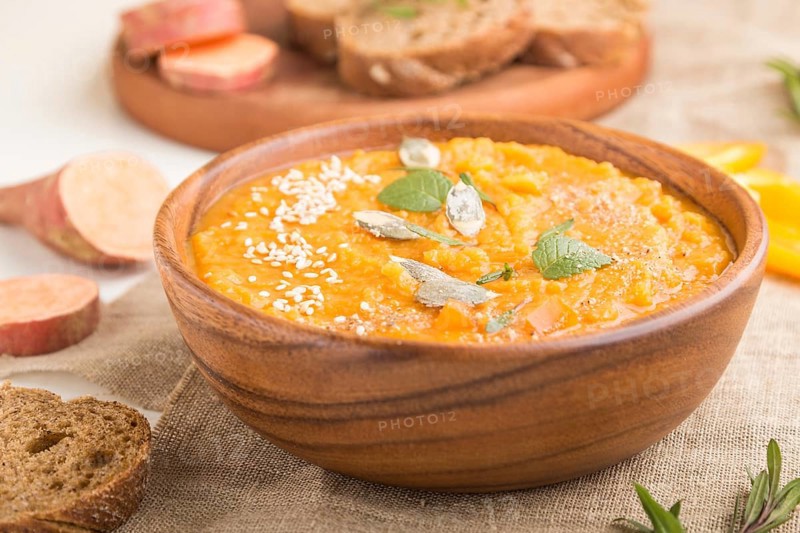 Sweet potato or batata cream soup with sesame seeds in a wooden bowl on a white wooden background with linen textile. side view, close up, selective focus