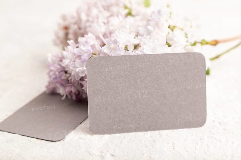 Gray business card with lilac flowers on gray concrete background. side view, copy space, mockup, template, spring, summer minimalism concept