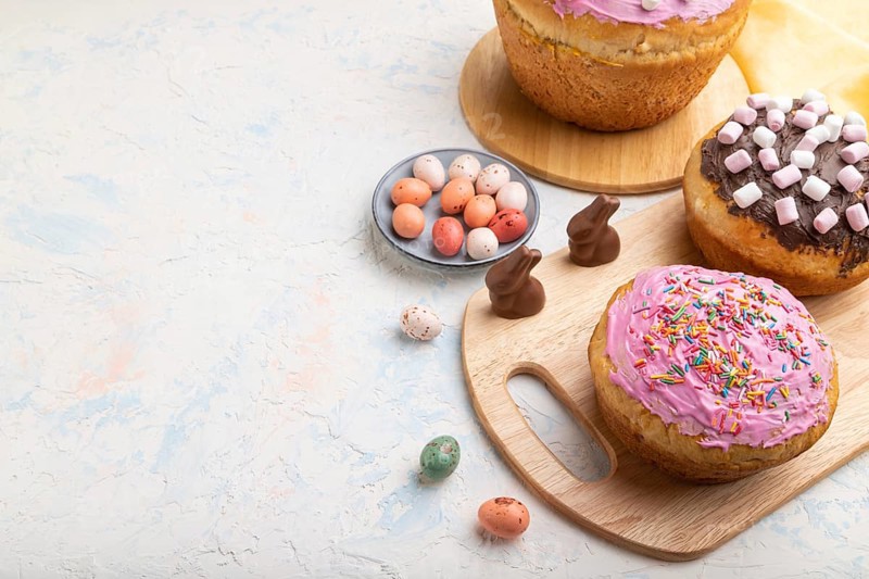 Homemade glazed and decorated easter pies with chocolate eggs and rabbits on a white concrete background and yellow textile. Side view, copy space