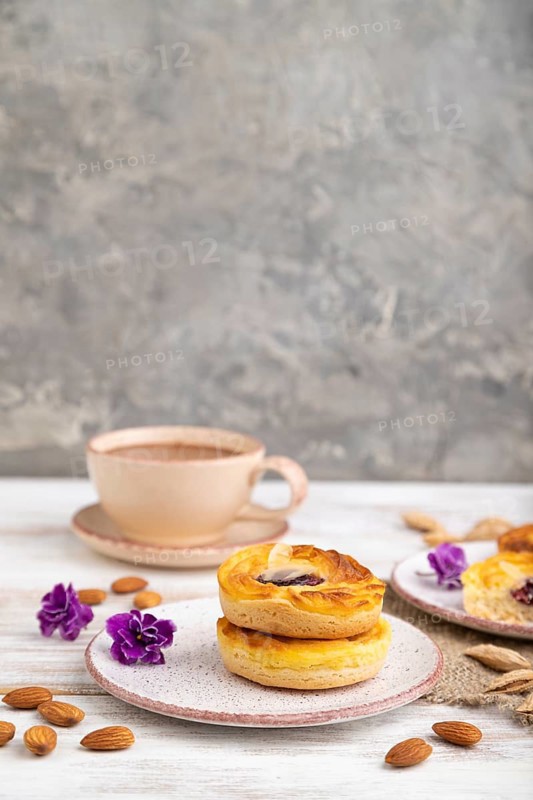 Small cheesecakes with jam and almonds with cup of coffee on a white wooden background and linen textile. Side view, copy space