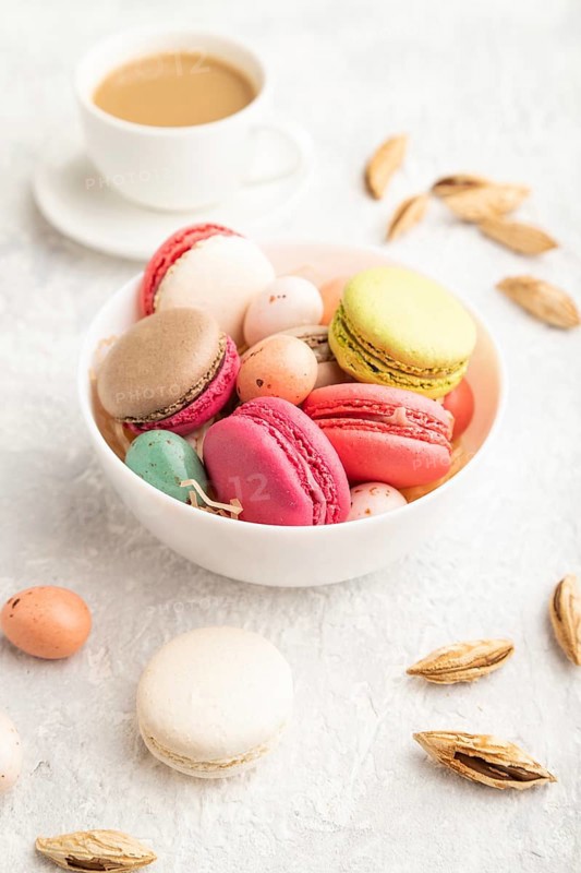 Multicolored macaroons and chocolate eggs in ceramic bowl, cup of coffee on gray concrete background. side view, close up, still life. Breakfast, morning, concept