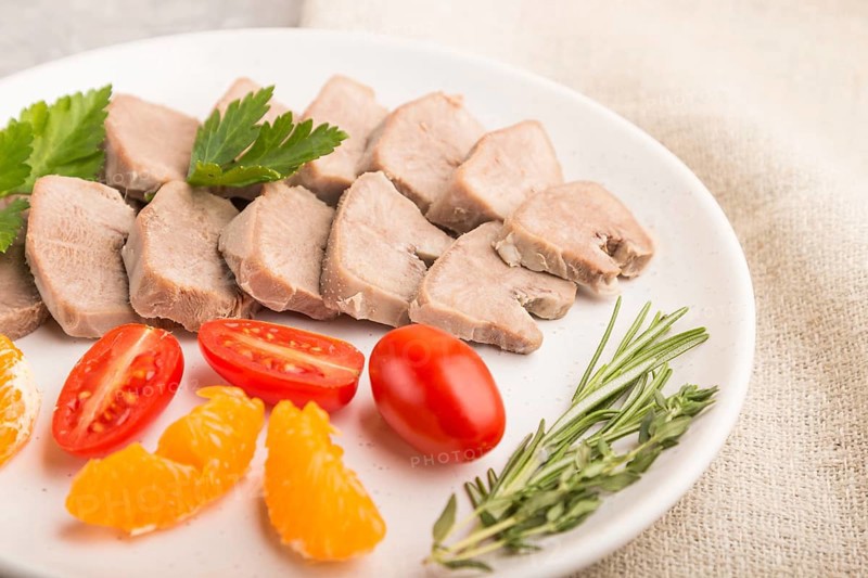 Boiled pork tongue with tomatoes and herbs on a gray concrete background and linen textile. Side view, close up, selective focus