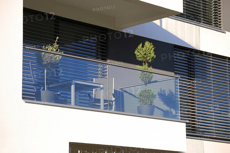 Balcony railing made of glass and stainless steel, behind it windows with modern blinds