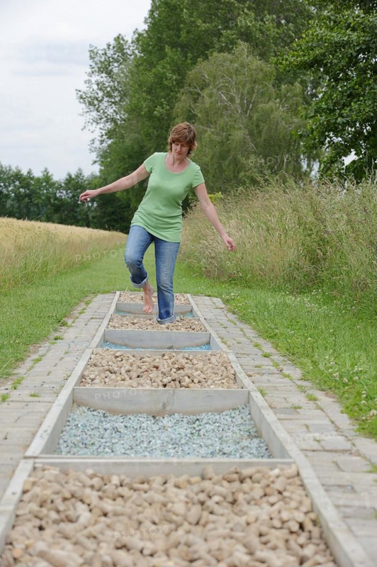 Woman walking barefoot over glass gravel and bottle corks, barefoot path Tilbeck Abbey, Havixbeck, North Rhine-Westphalia, Germany, Europe