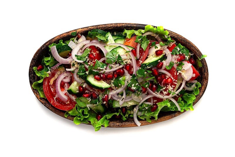 Salad of fresh vegetables, cucumbers, tomatoes, red onions, with nuts and pomegranate seeds, top view, in a clay plate, isolated
