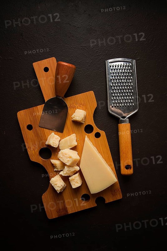 Hard cheese, parmesan, on a cutting board, cheese knife, grater, top view, no people