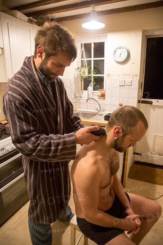 Young man shaving his brother's head home haircut in kitchen, UK, model released