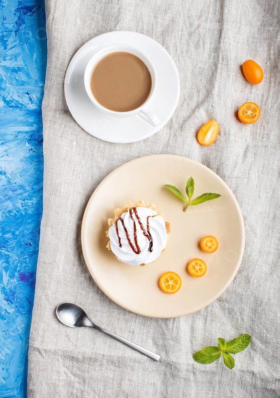 Cake with whipped egg cream on a light brown plate with kumquat slices and mint leaves on a blue concrete background with linen napkin. flat lay, top view