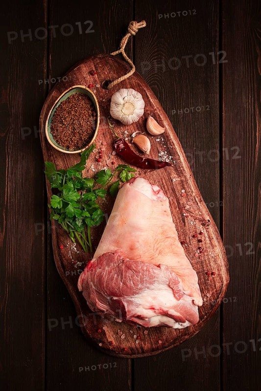 Raw pork knuckle, on a wooden chopping board, with spices, close-up, top view, no people