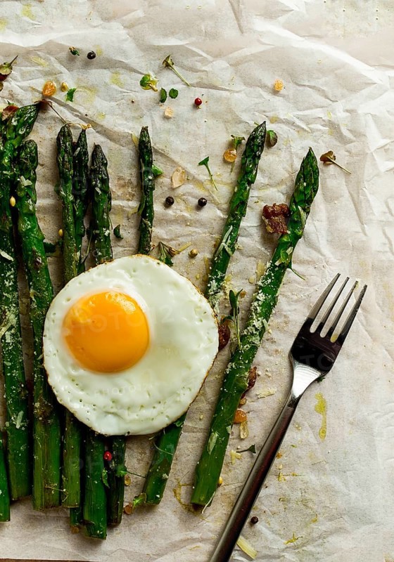 Grilled asparagus, with fried egg, spices and herbs, parmesan cheese, on a paper, top view, rustic, no people
