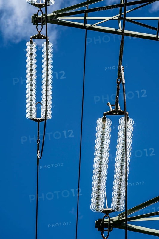 Insulators made of glass on a high-voltage line, they hang on the pylons as a suspension device between the pylon and the live, non-insulated cable, extra-high voltage line, symbolic image energy