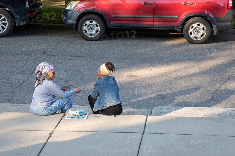 Detroit, Michigan, Two women sit on the curb outside the Shepherd art gallery during its grand opening