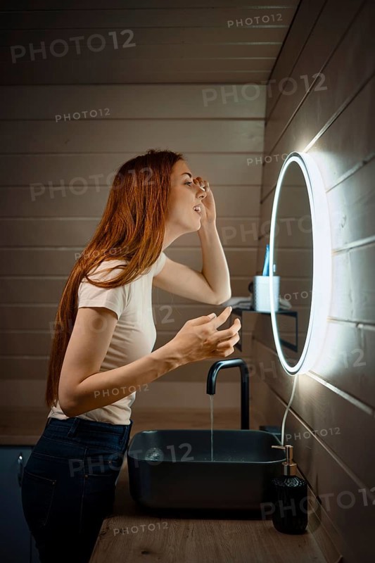 Young woman cleaning her face in washroom in the evening