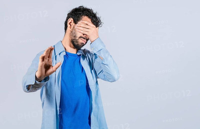 Scared confused man closing eyes with palm of hand isolated