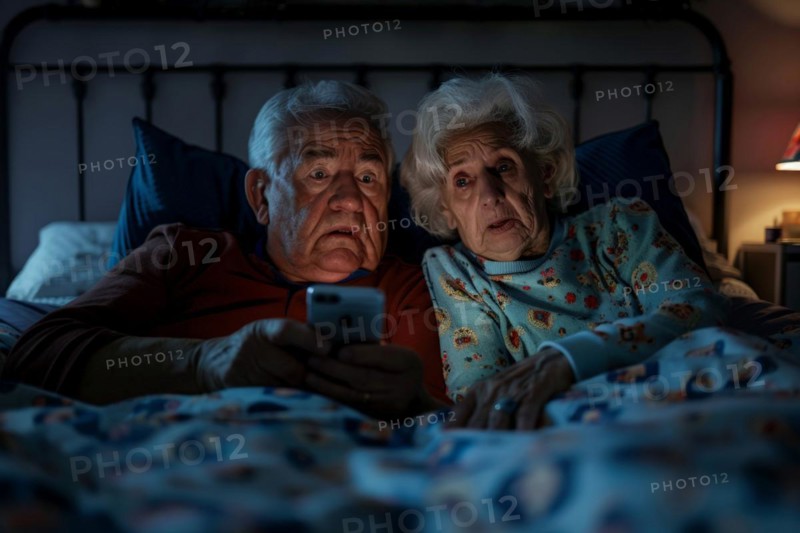 An elderly couple lies in their bedroom in their marital bed and looks at a smartphone, worried, frightened, unsettled, symbolic image for fraud against senior citizens, grandchild trick, shock calls, disclosure of personal data such as password, bank details, home address, media literacy, AI generated, AI generated, AI generated