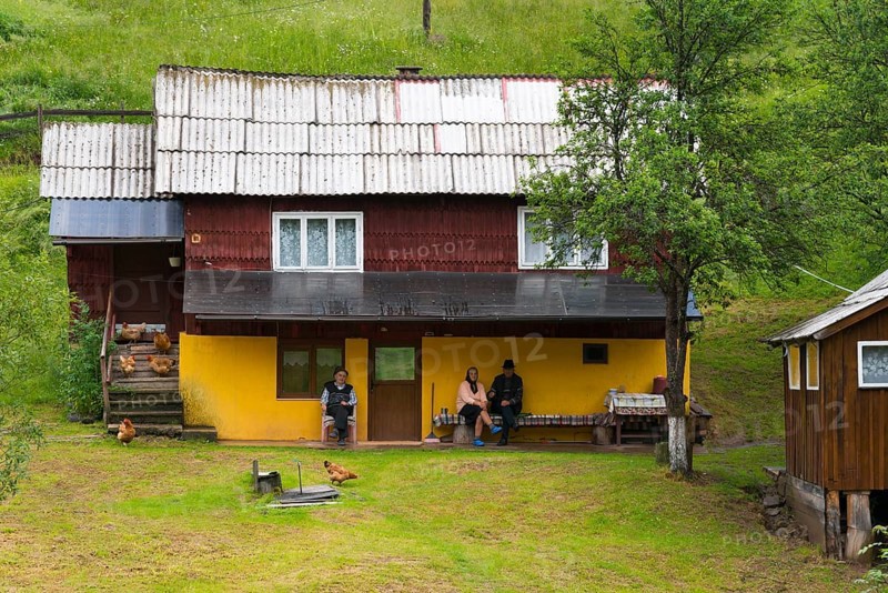 A yellow house surrounded by green grass with relaxed people and chickens in the front yard, Old people in front of a house, Bubesti, Alba, Transylvania, Romania, Europe
