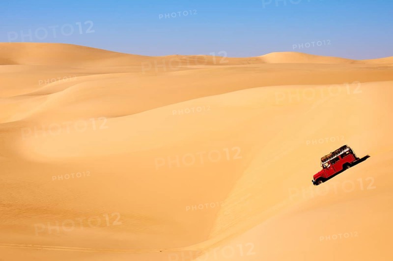 Off-road vehicle driving through vast sand dunes under a clear sky in a dry and sunny desert landscape, Matruh, Great Sand Sea, Libyan Desert, Sahara, Egypt, North Africa, Africa