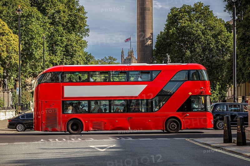 A red double-decker bus with a free advertising space or banner drives through a tree-lined street in London, United Kingdom, Europe