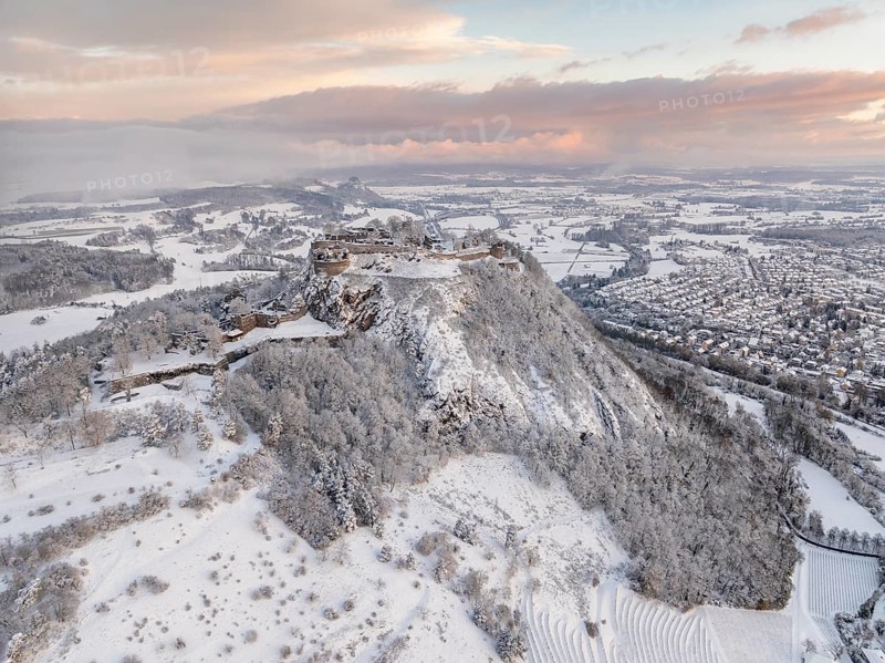 Aerial view of the snow-covered Hegau volcano Hohentwiel with Germany's largest castle ruin on a cold winter morning, in front of sunrise, surrounded by frosty trees in a winter landscape, on the horizon the neighbouring Hegau volcano Hohenkrähen, district of Constance, Baden-Württemberg, Germany, Europe