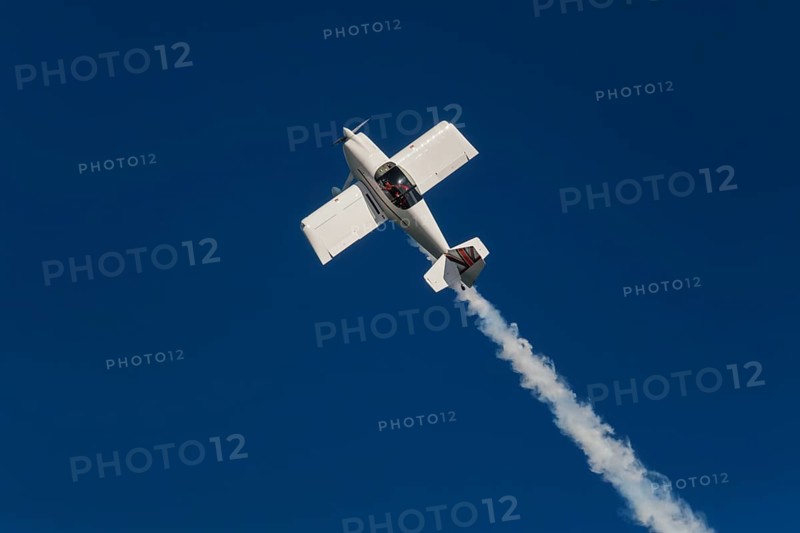 Stunt aerobatic plane performing stunts in blue sky with smoke trail. Concept of speed, difficulty, precision, risk, challenge