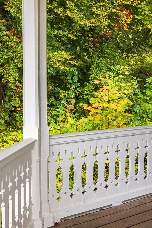 White wooden railing with joinery on a terrace with trees in autumn colours