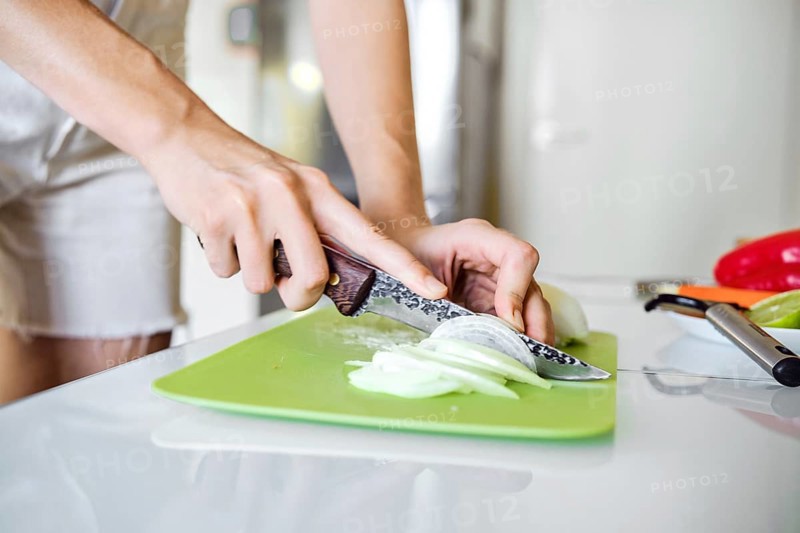 Close-up view of female hands chopping onion in a well-lit kitchen, slicing with precision on a cutting board