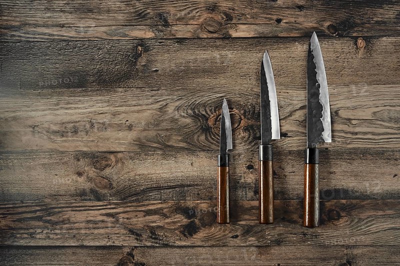 Three different types of kitchen knives are placed on a rustic wooden surface, showcasing their unique designs and polished blades