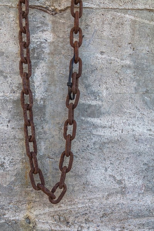 Close-up of heavy security chain with rusted links against a cement block background, Quebec, Canada, North America
