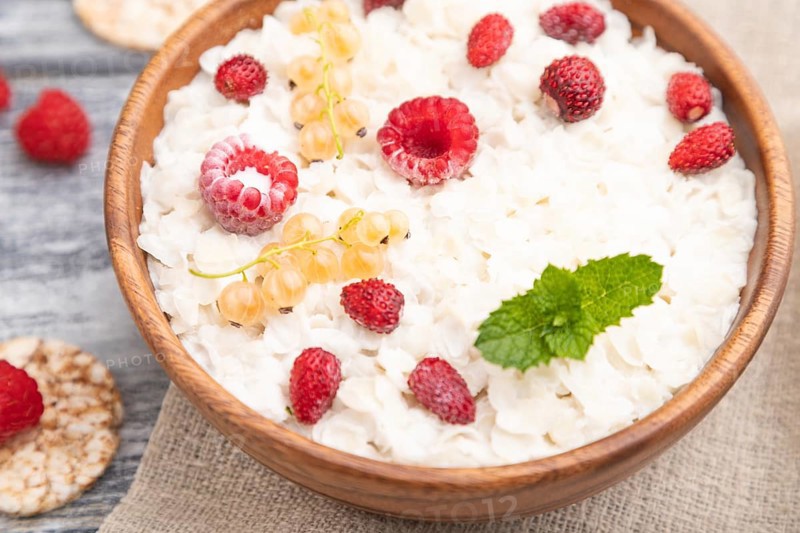 Rice flakes porridge with milk and strawberry in wooden bowl on gray wooden background and linen textile. Side view, selective focus, close up