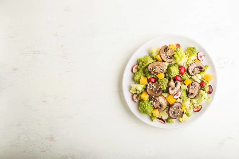 Vegetarian salad from romanesco cabbage, champignons, cranberry, avocado and pumpkin on a white wooden background and linen textile. top view, copy space, flat lay