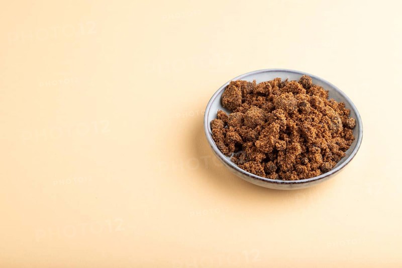 Plate with unrefined brown cane sugar on orange pastel background. side view, copy space