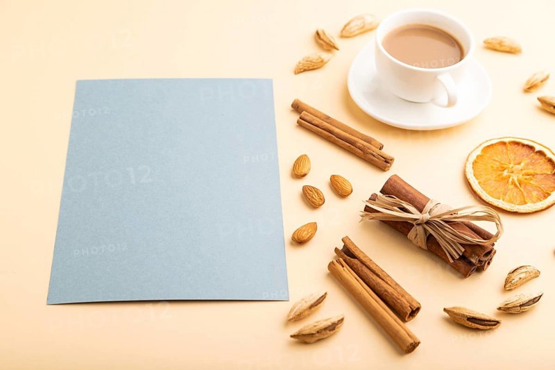 Composition with gray paper sheet, almonds, cinnamon and cup of coffee. mockup on orange background. Blank, side view, still life, copy space