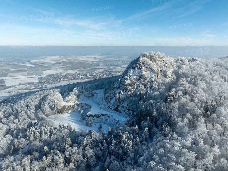 Aerial view of the snow-covered Hegau volcano Hohenstoffeln, with the former basalt quarry, surrounded by frosty trees in a winter landscape, behind it the village of Weiterdingen, district of Constance, Baden-Württemberg, Germany, Europe