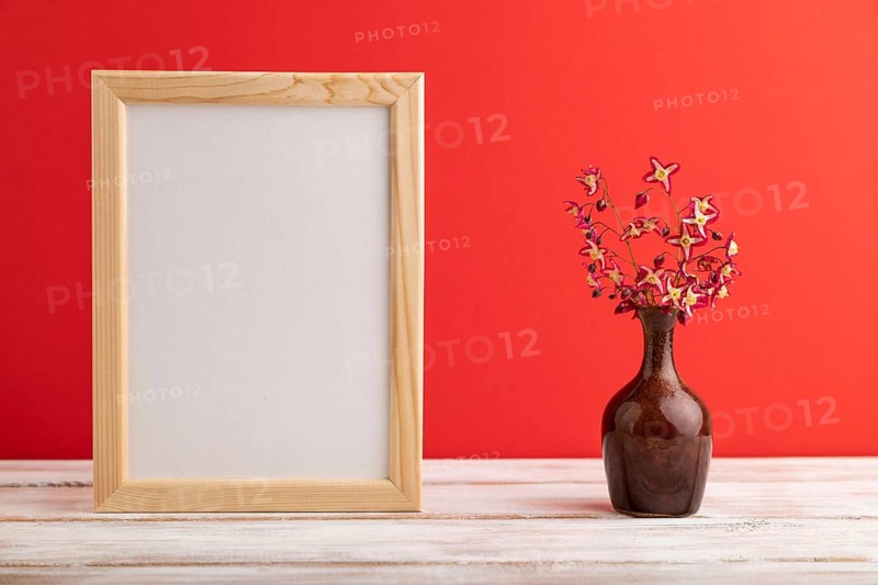 Wooden frame with purple barrenwort flowers in ceramic vase on red pastel background. side view, copy space, still life, mockup, template, spring, summer minimalism concept